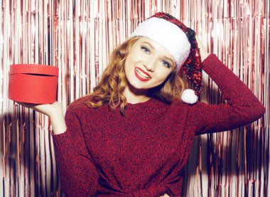 Parlak bir arka planda parlak bir Noel Baba şapkası takmış güzel bir kız