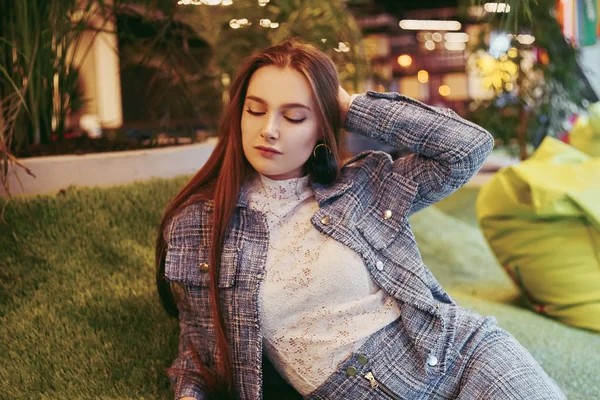 Kız kapalı alandaki yapay çimenlerin üzerinde yatıyor. İnekte dinlenen kız.