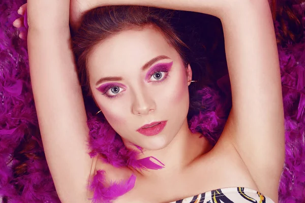 Modefoto eines Mädchens mit lila Make-up, liegt in blauer Feder — Stockfoto