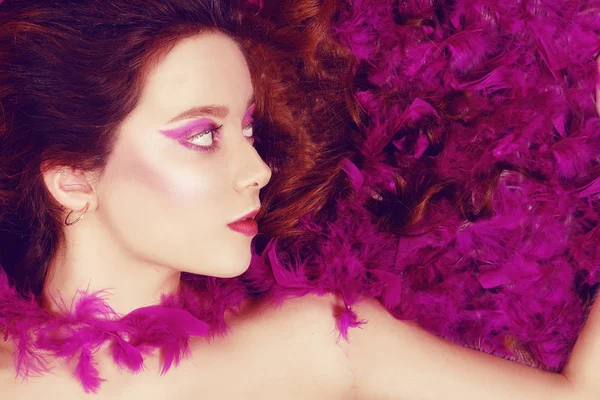 Beautiful young brunette lies with closed eyes in pink feathers. — Stock Photo, Image