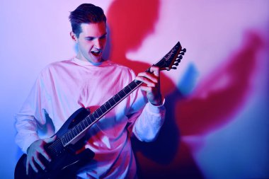 Şarkı söyleyen, çığlık atan, elektro gitar çalan genç bir sanatçının portresi, müzik konsepti. Rock Yıldızı neon ışıklı fotoğraf.