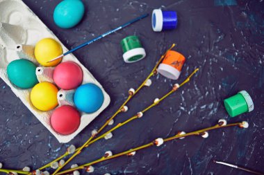 Mutlu Paskalyalar. Karton yumurtanın içinde renkli yumurta. Çiçekli söğüt çiçeği, koyu renkli soyut bir arka planda. Renkli boyalar, fırçalar, suluboya.