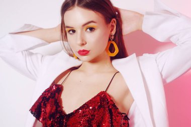 Parlak kırmızı elbiseli muhteşem bir esmer dans ediyor, beyaz ceketli bir model eğleniyor. Sarı aksesuarlı, küpeli ve pembe makyajlı bir kız..