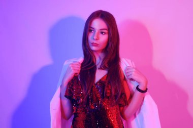 Kırmızı elbiseli, pullu, beyaz ceketli, gece kulübünde dans eden güzel bir esmer. Neon ışıklı kız. Metin için alanı kopyala.