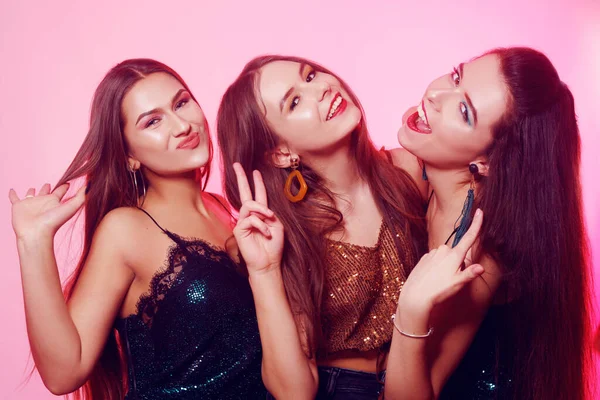 3 girls pose, make faces, show tongue. Girls in brilliant dresses with different colorful makeup. Three brunette girls dance and enjoy life. March 8, women\'s power, Women\'s Day.