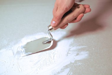 Bir adam duvara tükürüyor. Macun. Bir adamın eli bir spatulayı tutuyor. onarım işi..