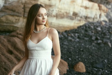 Sahilde okyanusta uzun beyaz elbiseli güzel bir kız. Model doğa tarafından miras alınmıştır. Tatildeki kız, hafif elbise, yaz tatili, moda. Rüzgarda muhteşem uzun saçlar gelişiyor. Tenerife