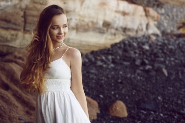 Sahilde okyanusta uzun beyaz elbiseli güzel bir kız. Model doğa tarafından miras alınmıştır. Tatildeki kız, hafif elbise, yaz tatili, moda. Rüzgarda muhteşem uzun saçlar gelişiyor. Tenerife