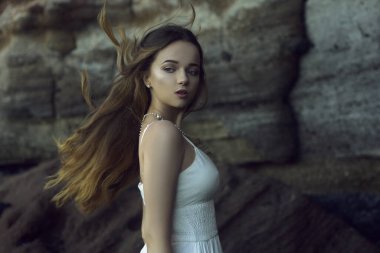 Sahilde okyanusta uzun beyaz elbiseli güzel bir kız. Model doğa tarafından miras alınmıştır. Tatildeki kız, hafif elbise, yaz tatili, moda. Rüzgarda muhteşem uzun saçlar gelişiyor. Tenerife