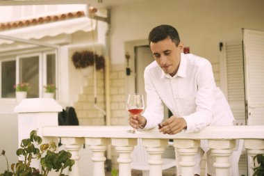 Bir adam terasta duruyor ve puro içiyor, kırmızı / pembe şarap içiyor. Zengin bir adam okyanustaki bir evde dinleniyor. Yalnız seyahat etmek, diye düşündü adam. Beyazlı bir adam tatilde..