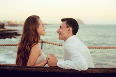 Bir çift okyanusun arka planında oturur, sarılırlar, öpüşürler. Dinlenme, tatil, seyahat, balayı konsepti. Bir kız ve bir erkek bir bankta oturuyor, okyanusun ve dağların arkasında dinleniyorlar..