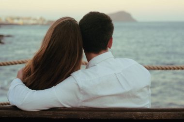 Bir çift okyanusun arka planında oturur, sarılırlar, öpüşürler. Dinlenme, tatil, seyahat, balayı konsepti. Bir kız ve bir erkek bir bankta oturuyor, okyanusun ve dağların arkasında dinleniyorlar..