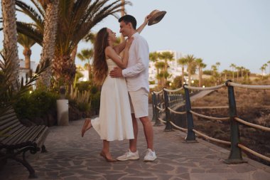 Okyanus kıyısında palmiye ağaçlarının arka planında gezinen bir çift. Beyaz randevulu bir adamla birlikte uzun beyaz elbiseli bir kız. Balayı, seyahat, turizm, Kanarya Adaları.