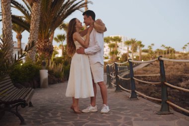 Okyanus kıyısında palmiye ağaçlarının arka planında gezinen bir çift. Beyaz randevulu bir adamla birlikte uzun beyaz elbiseli bir kız. Balayı, seyahat, turizm, Kanarya Adaları.