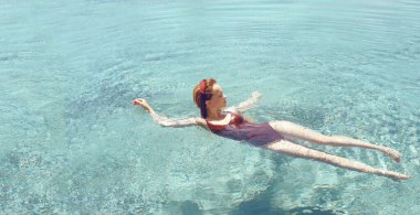 Mutlu kız havuzda yüzer. Havuz manzaralı bir kız, kırmızı mayo giymiş şık bir kız rahatlıyor. Seyahat, dinlenme, güneş, yaz.