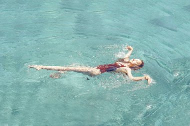 Mutlu kız havuzda yüzer. Havuz manzaralı bir kız, kırmızı mayo giymiş şık bir kız rahatlıyor. Seyahat, dinlenme, güneş, yaz.