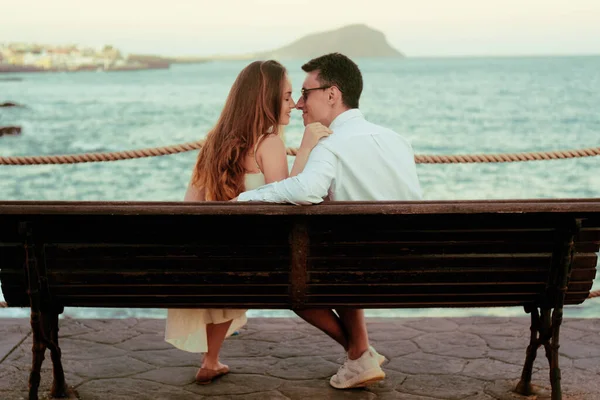 夫婦は海 キスの背景に座っている 新婚旅行の概念 海と山を背景にリラックスしてベンチに座っている女の子と男 — ストック写真
