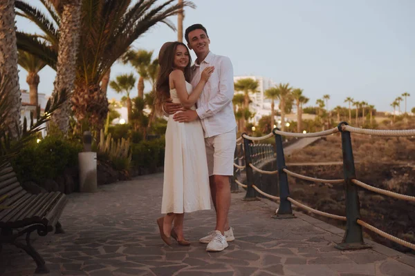 一对夫妇在海边的棕榈树下散步 穿着白色长裙的女孩和一个穿白色约会衣服的男人在一起 加那利群岛 — 图库照片