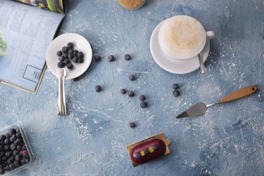 İnanılmaz güzel kırmızı bordo tatlı ve yabanmersini. Tabakta yabanmersini. Kahveli latte kahvaltı. Mavi yaratıcı bir altyapının taslağı. Kahvaltının muhteşem fotoğrafı, şekerler. Eğitim fotoğrafı..