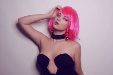 Beyaz arka planda bir kız, profesyonel model. Pembe saçlı kız, gizemli, güzel, kameraya bakıyor, flört ediyor, flört ediyor. Uzun pembe küpeler. İnanılmaz bir bakış..