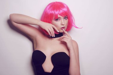 Beyaz arka planda bir kız, profesyonel model. Pembe saçlı kız, gizemli, güzel, kameraya bakıyor, flört ediyor, flört ediyor. Uzun pembe küpeler. İnanılmaz bir bakış..