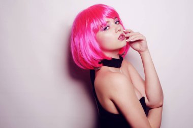 Beyaz arka planda bir kız, profesyonel model. Pembe saçlı kız, gizemli, güzel, kameraya bakıyor, flört ediyor, flört ediyor. Uzun pembe küpeler. İnanılmaz bir bakış..