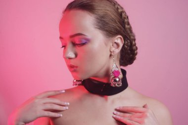 Aksesuarlı doğal bir kız. Güzel, profesyonel saç örgüsü olan bir kız. Pembe arka planda güzel pembe makyajlı bir kız. İlginç bir görüntü. İlginç ışığı olan bir kızın portresi..