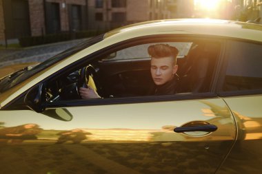 Pahalı bir araba süren bir adam. Bir adam kullanıyor, başarılı bir adam araba sürüyor. Altın sarısı araba. Gün batımında araba kullanan bir adam. Başarı, pahalı, serbest, iş adamı, ünlü.