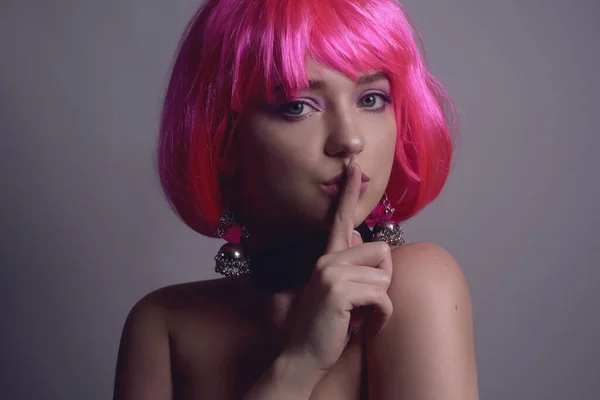 Portrait of a girl with pink hair and chic, fashionable earrings, pink earrings with silver. Jewelry, accessories. The girl shows a gesture of silence. Girl tells a secret. Hush.