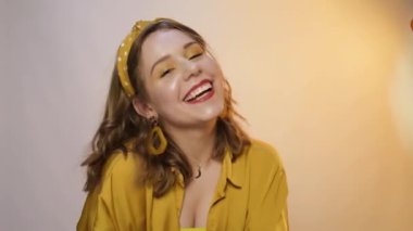 Sarı ışıkta sevimli bir kız, gülüyor, gülümsüyor ve kameraya bakıyor. Aksesuarları ve kafasında bir çember olan bir genç..