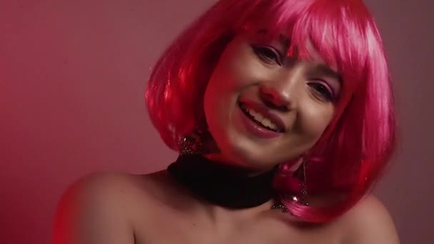粉红短发的女孩 一个有着长长的粉色耳环和化妆品的模特 视频中的女孩笑了 摆姿势 摸她的头发 发疯了 时尚视频肖像 — 图库视频影像