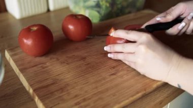 Bir kızın elleri domatesleri küp küp doğradı. Kız evde yemek pişiriyor. Oyunculuk kurulu, bir kız domatesi dilimler..