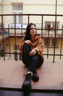 Bir kız balkonda duruyor. Esmer kadın nefes almak, şarap içmek ve havanın tadını çıkarmak için balkona çıktı. Karantina, balkon rahatlamak için bir yer. Çiçekler ve bahar.