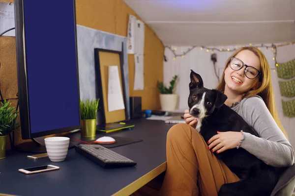 A girl with a dog is sitting at home near her desktop. The girl in between freelance work is played with a dog. A girl learns at home, a dog in her arms. Computer green screen