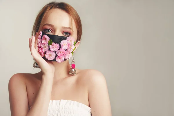 Fashion photo of a girl in a mask of flowers. Spring that we cannot breathe. Virus, pandemic, coronavirus, masked model, beauty model in a mask of fresh pink flowers. Girl with a delicate pink make-up.