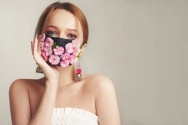 Çiçek maskeli bir kızın moda fotoğrafı. Nefes alamadığımız bahar. Virüs, salgın hastalık, koronavirüs, maskeli manken, taze pembe çiçeklerden oluşan bir maskeli güzellik modeli. Narin pembe makyajlı kız..