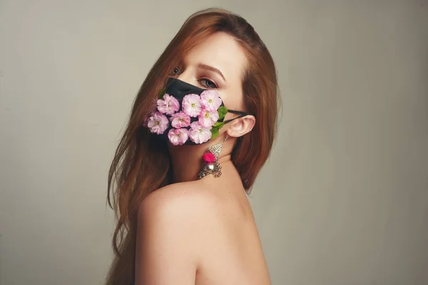 Girl with gorgeous long hair in an antiviral mask. Fashion photo on the cover of the magazine. Pandemic, virus, coronavirus, masked girl spring has come. Spring fashion, model in a mask of flowers