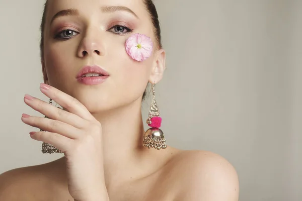 Girl with a gentle make-up and a flower on her face. Delicate skin, skin care in the spring. Spoil the model, spring, flowering, beauty and personal care. A close-up of a pink tender flower on the girl\'s face.