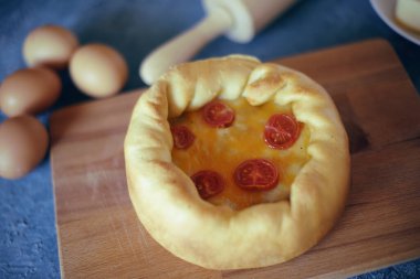 Derin Tabak Pizzası. Hicago pizza peynirleri, kurutulmuş kiraz domatesleri. Tahta tabakta yemek, merdane ve yumurta, peynir, malzemeler... Mavi arkaplanda hamur işi.