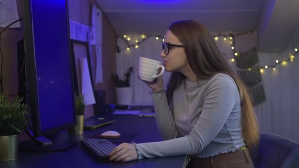 这个女孩在家里的电脑边工作 屏幕是蓝色的 绿色的 女孩戴上眼镜 开始做自由职业者 看着屏幕 在键盘上打字 然后用鼠标 — 图库视频影像