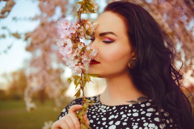 Sakura 'nın arka planında şık bir kız, pembe çiçekler, ağaç. Pembe makyajlı esmer, bahar. Alerjisi olmayan bir kız çiçek açar. Güzel bir kız portresi..