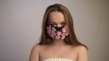 Antiviral maskeli, uzun saçlı, muhteşem bir kız. Moda videosu. Salgın, virüs, koronavirüs, maskeli kız baharı geldi. Bahar modası, çiçekli bir maskenin içindeki model..