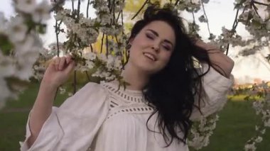 Parkta, ağaçların yanında çiçekli bir kız. Beyaz boho elbiseli bir esmer, alerjisi olmayan, çiçekleri kokan doğa tarafından yatırılır..