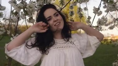 Parkta, ağaçların yanında çiçekli bir kız. Beyaz boho elbiseli bir esmer, alerjisi olmayan, çiçekleri kokan doğa tarafından yatırılır..