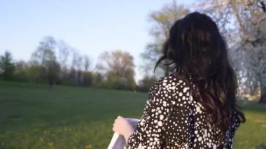 Parktaki beyaz ceketli kız poz veriyor, yürüyor ve kameraya bakıyor. Çiçekler, beyaz çiçekli ağaç dalları. Güzel bahar, ağaçlar çiçek açıyor..