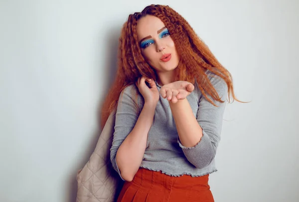 A girl with curled voluminous hair is dancing, a model in the style of the 80s. 90s, with bright blue make-up and a jacket. Girl on a white background. Model blows a kiss