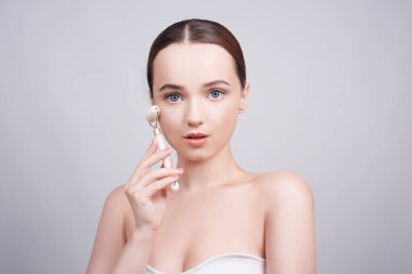 Doğal beyaz kuvars yüz silindiri kullanırken rahat görünen genç bir kadının portresi. Güzellik yüz bakımı. Kadın evde yüz masajı yapıyor. Yeşim yüz silindirleriyle kaplıca tedavisi için.. 