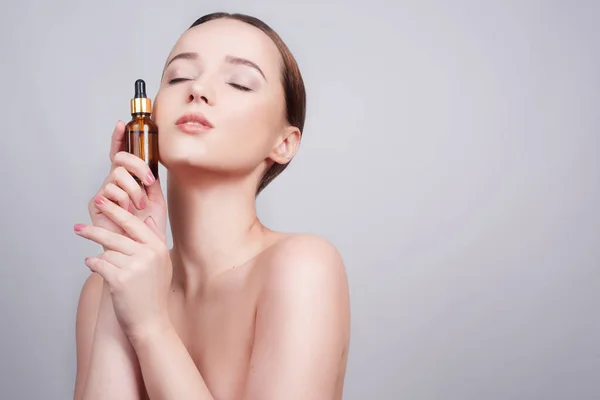 Yüzünde kozmetik yağlı pipetle model esmer kıza yakın çekim. Güzellik terapisi konsepti. Mavi gözlü manken gülümsüyor, cilt bakımı. 