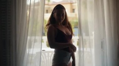 Yazın muhteşem uzun saçlı kız beyaz perdeleri ve danslarıyla pencereye doğru yürür. Sıcak bir ülkede sabah, kısa şortlu, uzun saçlı bir kız dans ediyor. Seksi kız.