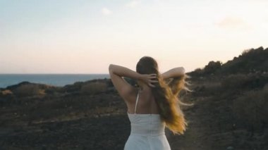 Gün batımında bir kız yaz adası boyunca yürür. Uzun saçlı hassas bir kız dağlarda beyaz bir elbiseyle yürüyor. Okyanusun arka planında bir model, sakin, sessiz.